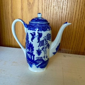 May include: A white and blue ceramic teapot with a lid. The teapot features a classic blue and white Willow pattern design. The handle and spout are white, and the lid has a small knob. The teapot is likely vintage and is a decorative item.