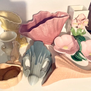 May include: A collection of vintage ceramic vases and bowls in various colors and shapes, including pink, yellow, blue, and brown. The vases feature floral designs and unique forms.