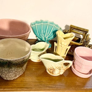 May include: A collection of vintage ceramic planters and vases in various colors and styles. The planters include a green and brown planter with a crackled glaze, a light green planter with a basket design, a pink planter with a ribbed design, and a brown planter with a well design. The vases include a yellow vase with a floral design, a light blue vase with a fan design, and a pink vase with a ribbed design.
