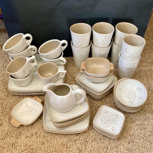 May include: A set of white ceramic teacups and saucers with a brown floral design. The set includes a creamer, sugar bowl, and teacups.