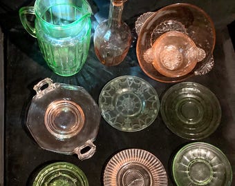 May include: A collection of vintage glassware in shades of green and pink. The assortment includes a pitcher, a decanter with a stopper, saucers, and bowls. The glass pieces have various patterns and shapes, showcasing a classic aesthetic.