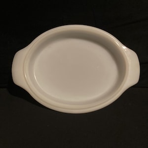 May include: A white, oval-shaped casserole dish with two handles. The dish has a smooth, glossy finish and a simple, classic design. It is likely made of ceramic or glass and is suitable for baking and serving.