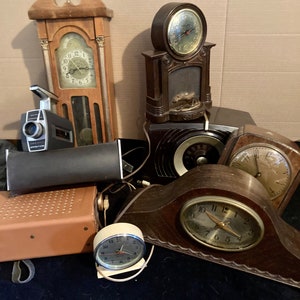 May include: A collection of vintage clocks, including a grandfather clock, a mantle clock, and a small alarm clock. The clocks are all in various styles and colors, and they are all in working order.