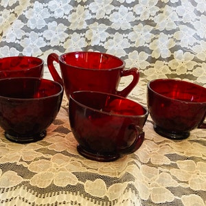 May include: Set of five red glass cups, including a larger pitcher, with a textured surface. The cups have a rounded shape and a handle on one side.