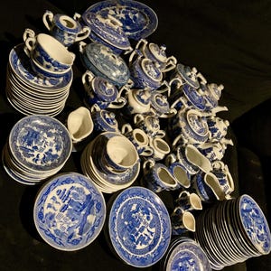 May include: A collection of blue and white porcelain dishware, including plates, teacups, saucers, teapots, and creamers. The pieces feature a classic Willow pattern design. The arrangement suggests a complete tea set.