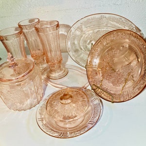 May include: A set of vintage pink Depression glass, including a covered dish, butter dish, three glasses, and two plates. The glass features a floral pattern.