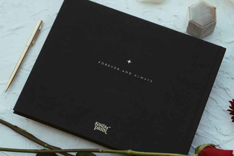 May include: A black book with the words "FOREVER AND ALWAYS" and a star printed on the cover. A gold pen, a gray ring box, and a red rose are also visible. The book has the "Sugar Plum" logo.
