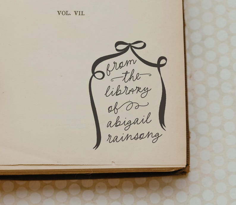 Peut inclure: Un livre avec le texte "Vol. VII" sur la couverture. Une inscription manuscrite indique "from the library of abigail rainsong" avec un motif de ruban d&eacute;coratif.