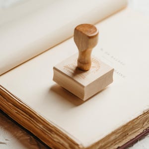 May include: A wooden stamp with a design on the top, sitting on an open book with aged pages.