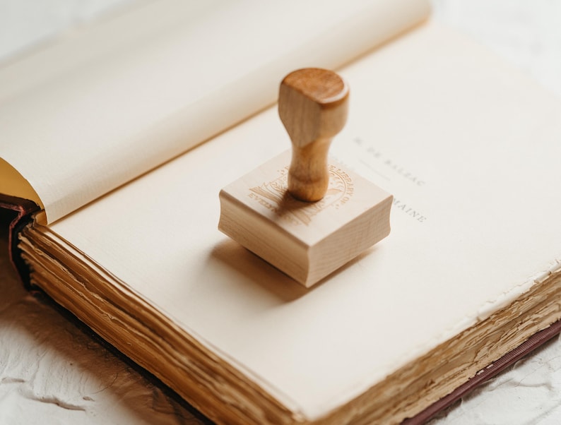 May include: A wooden stamp with a design on the top, sitting on an open book with aged pages.