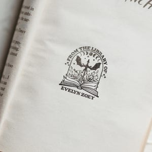 May include: A black and white book stamp with a dragon, moon, and stars. The text reads "From the Library of Evelyn Zoey."
