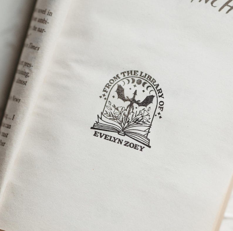 May include: A black and white book stamp with a dragon, moon, and stars. The text reads "From the Library of Evelyn Zoey."