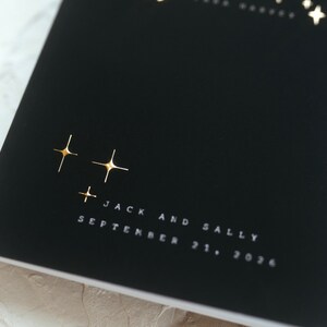 May include: Black invitation with gold foil star details. The text "Jack and Sally" and the date "September 21, 2036" are printed in white. The invitation has a minimalist design, suitable for a wedding.