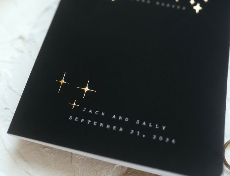 May include: Black invitation with gold foil star details. The text "Jack and Sally" and the date "September 21, 2036" are printed in white. The invitation has a minimalist design, suitable for a wedding.