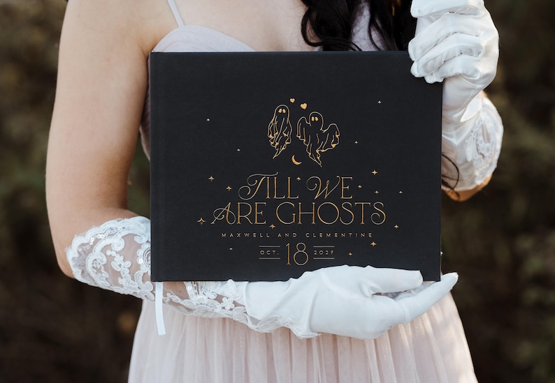 May include: Black book with gold lettering and illustrations. The cover reads "Till We Are Ghosts" with ghost and star illustrations. The book also includes the names "Maxwell and Clementine" and the date "Oct. 18 2021".