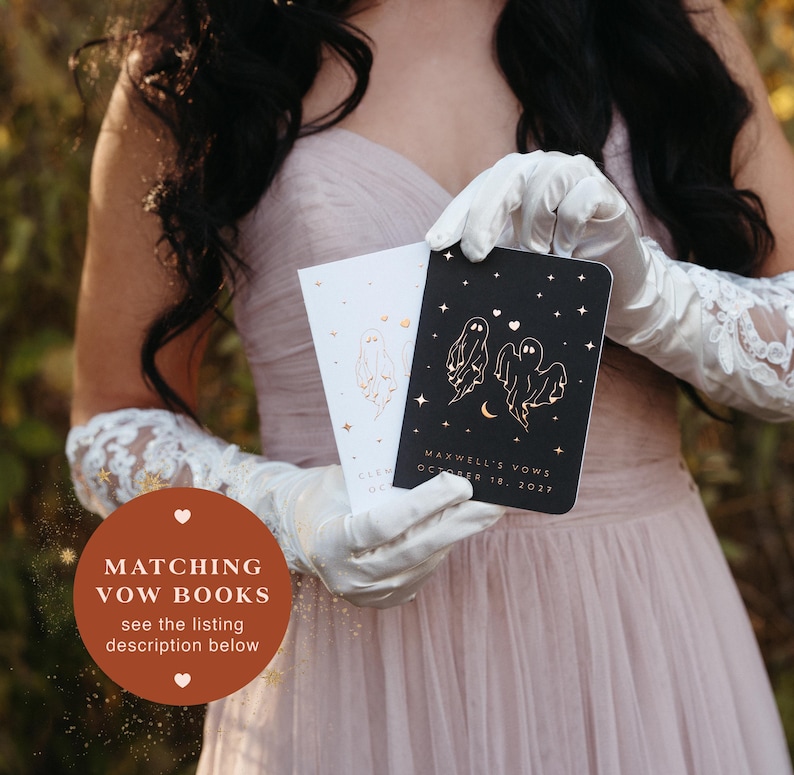 May include: Two vow books are held in white gloves. One book is black with gold ghost illustrations and the text "MAXWELL'S VOWS OCTOBER 18, 2027". The other book is white with a gold ghost illustration. The text "MATCHING VOW BOOKS see the listing description below" is in the image.