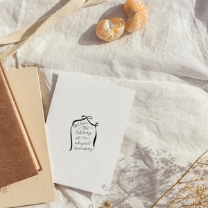 Peut inclure: Une carte blanche avec une calligraphie noire qui dit "from the library of abigail rainsong". La carte est sur une surface en tissu blanc avec un livre brun et quelques fleurs s&eacute;ch&eacute;es.