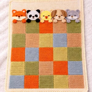 Peut inclure: Une couverture pour bébé au crochet avec un motif patchwork de carrés orange, verts, jaunes et bleus. La bordure est de couleur crème et le bord supérieur présente cinq visages d'animaux au crochet : un renard, un panda, un poussin, un chien et un chat.