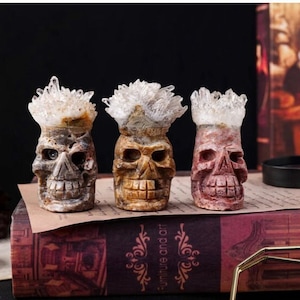 Pode incluir: Três estatuetas de caveira de cristal esculpidas com detalhes em cristal branco. As caveiras são de diferentes cores: marrom, bege e rosa.