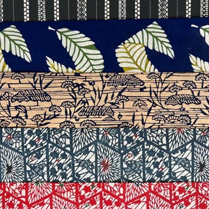 May include: Five fabric swatches featuring a variety of Japanese-inspired designs. The top swatch is black with white stripes and dots. The second swatch is dark blue with white and green leaf patterns. The third swatch is peach with black floral and geometric patterns. The fourth swatch is dark blue with white and red geometric patterns. The bottom swatch is red with white and green geometric patterns.
