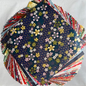 Peut inclure: Un &eacute;ventail de carr&eacute;s de papier aux motifs color&eacute;s, avec un carr&eacute; bleu fonc&eacute; avec un motif floral blanc et or au centre.
