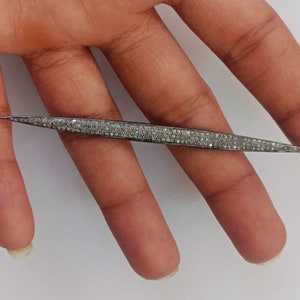 May include: A long, slender, pointed metal jewellery component with a dark, oxidised finish, densely encrusted with numerous small, sparkling white stones along its entire length, featuring a small circular loop at one end for attachment.