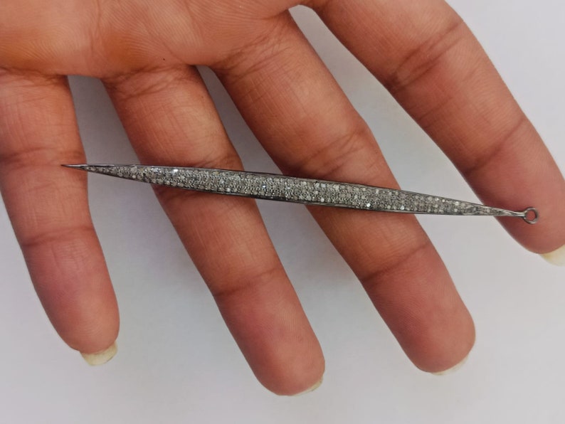 May include: A long, slender, pointed metal jewellery component with a dark, oxidised finish, densely encrusted with numerous small, sparkling white stones along its entire length, featuring a small circular loop at one end for attachment.