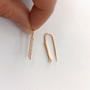 Puede incluir: Dos ganchos para pendientes de oro, uno con una fila de piedras de cristal transparentes y el otro con una barra lisa.