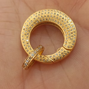 May include: A gold-toned clasp with a round, pave-set design. The clasp is made of two pieces that fit together.