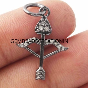 May include: Black oxidized silver charm with a bow and arrow design. The arrow is tipped with a triangle and both the bow and arrow are accented with clear cubic zirconia stones.