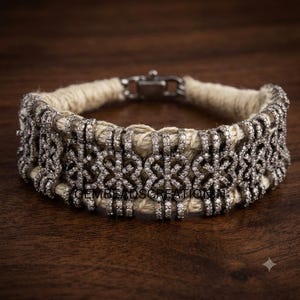 Può includere: Un bracciale con una base in corda di juta intrecciata color beige, avvolta da maglie in metallo color argento. Ogni maglia è incastonata con piccole pietre chiare e scintillanti in un motivo floreale ripetuto, completo di una chiusura in metallo.