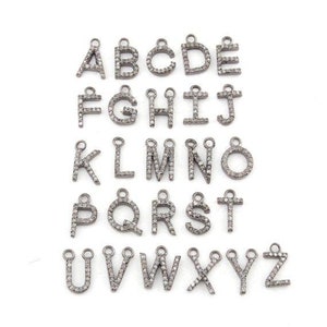 May include: A set of silver alphabet charms, each with a small loop for attachment. The letters A to Z are shown, each encrusted with small, sparkling embellishments. The charms are arranged on a white background.