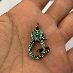 May include: A silver clasp with a green crystal design. The clasp is round and has a small loop on the side.