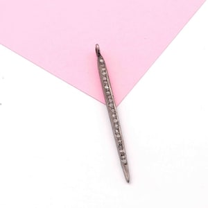 Puede incluir: Un colgante de plata con forma larga, delgada y puntiaguda. El colgante está decorado con una fila de pequeños diamantes transparentes.