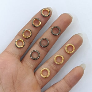 May include: A collection of small, round, gold and silver rings with clear and black gemstones. The rings are arranged on a hand.