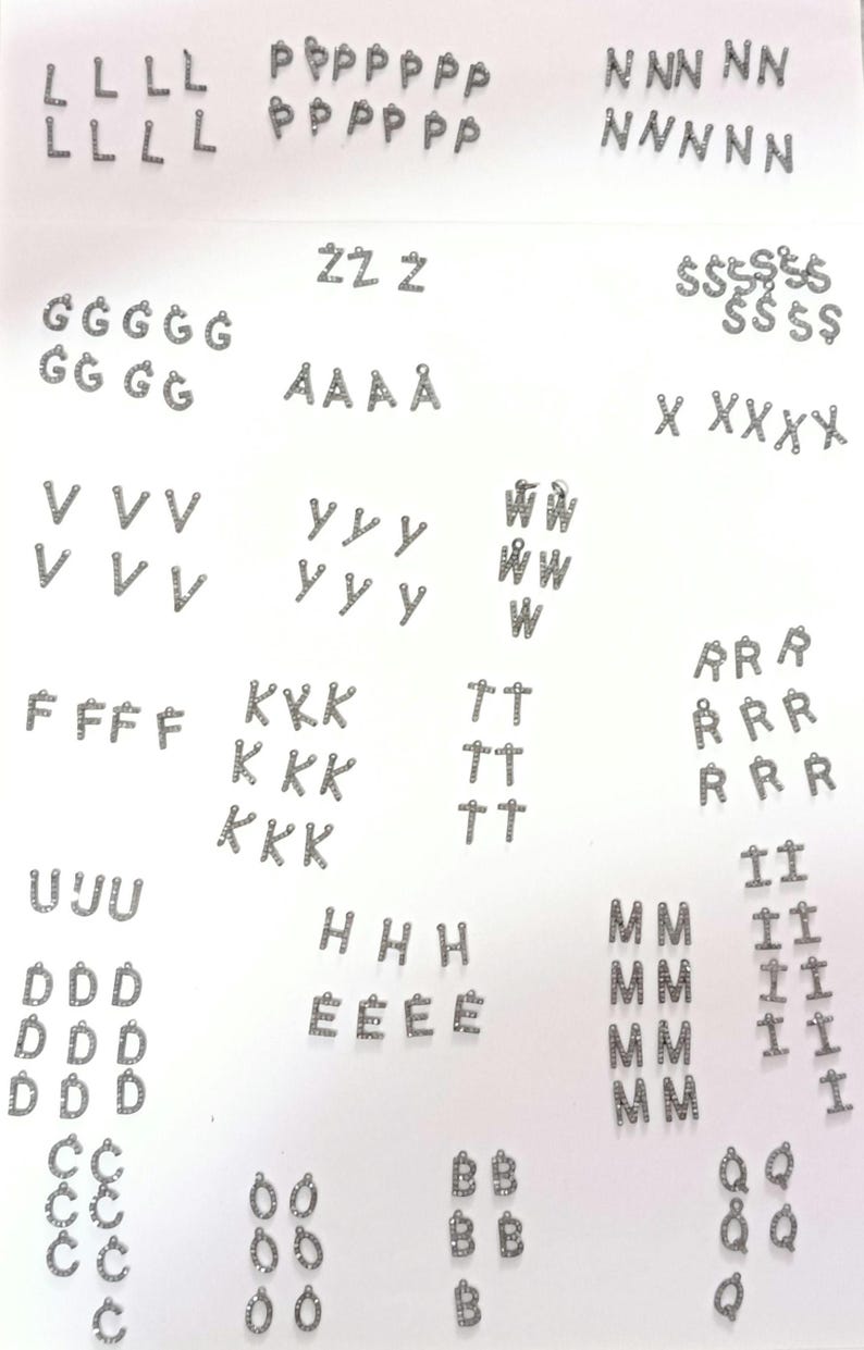 May include: A selection of silver-coloured letter charms, including the letters L, P, N, Z, G, A, V, W, X, F, K, T, R, U, H, E, M, I, Q, D, C, and B. Each charm is small and has a loop for attaching to jewellery.