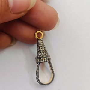 May include: A silver and gold pendant with a teardrop shape and a cone-shaped top. The pendant is covered in small, clear diamonds.