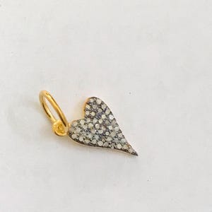 May include: A gold charm in the shape of a heart with a pave setting of small white diamonds.