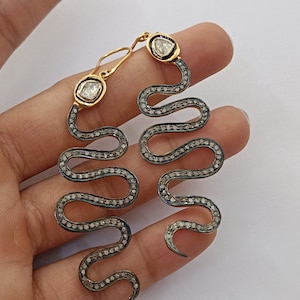 May include: A pair of silver snake earrings with pave diamond accents and a single diamond at the top of each snake. The earrings are dangling and have a gold hook closure.