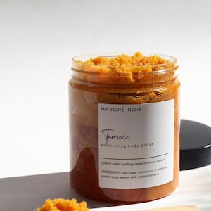 May include: A glass jar of turmeric exfoliating body polish with a black lid. The jar is filled with a bright orange scrub. The label reads "MARCHÉ NOIR Turmeric exfoliating body polish". The label also includes the usage and ingredients: "USAGE: while bathing, apply in circular motions INGREDIENTS: raw sugar, coconut oil, avocado oil, castile soap, epsom salt, organic turmeric"