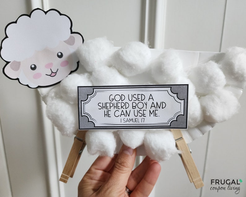 May include: A white paper plate craft depicting a sheep with cotton balls for wool. A gray sign with the text "GOD USED A SHEPHERD BOY AND HE CAN USE ME. I SAMUEL 17" is attached to the sheep with wooden clothespins.