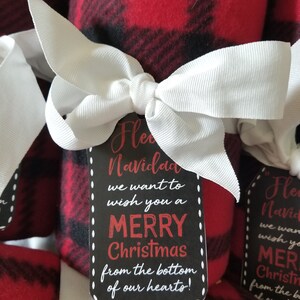 May include: Rolled red and black plaid fleece blankets tied with white ribbon bows. Each blanket has a black tag with the words "Merry Christmas" in red and white text.