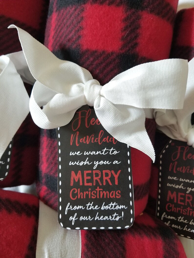 May include: Rolled red and black plaid fleece blankets tied with white ribbon bows. Each blanket has a black tag with the words "Merry Christmas" in red and white text.