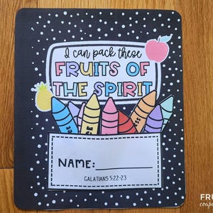 May include: A black notebook cover with white polka dots and colourful illustrations. The text "I can pack these FRUITS OF THE SPIRIT" is displayed above a crayon design. Below is a space for a name and the scripture reference Galatians 5:22-23.