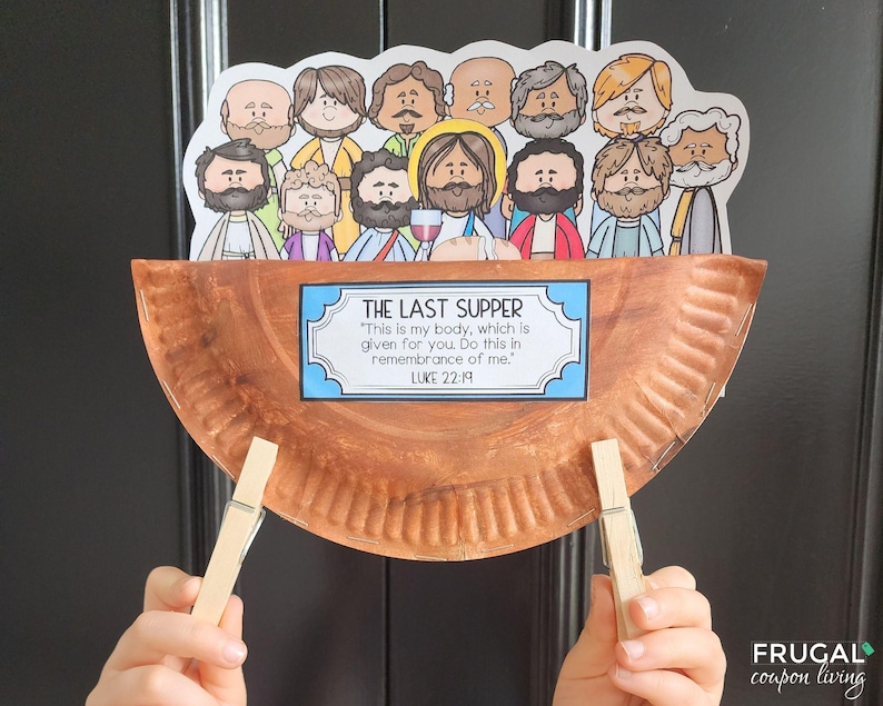 May include: A brown paper plate with a scalloped edge is decorated with a blue and white sign that reads "The Last Supper" and a quote from Luke 22:19.  The plate is held up by two wooden clothespins.  The plate is decorated with cartoon images of people, including Jesus, at the Last Supper.