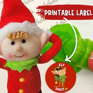 Könnte beinhalten: Eine Plüsch-Elf-Puppe in roter Kleidung mit weißer Verzierung und einem grünen Kragen. Das Bild zeigt eine grüne Flasche und ein rotes rundes Etikett mit dem Text "ELF SNOT". Die Worte "PRINTABLE LABELS" stehen in einem roten Banner.