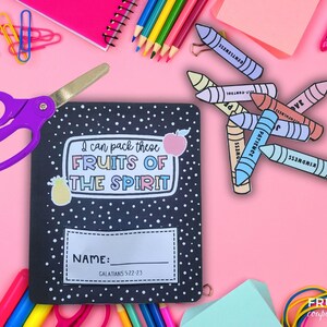May include: A black notebook with white polka dots and the text "I can pack these FRUITS OF THE SPIRIT" is surrounded by school supplies. A pair of purple scissors, colourful crayons, and pencils are scattered on a pink background.