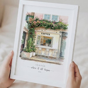 May include: A framed watercolor print of a coffee shop with the word "COFFEE" above the window. The print includes the text "Lily & Noah where it all began 2024". The shop is decorated with flowers and cacti.