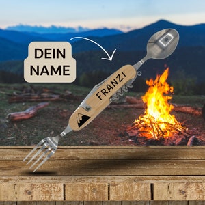Könnte beinhalten: Ein personalisiertes Camping-Besteck mit einem Holzgriff und einer Gabel, einem Löffel und einem Flaschenöffner aus Metall. Der Griff ist mit dem Text "FRANZI" und einem Bergmotiv graviert. Das Besteck liegt auf einer Holzoberfläche vor einem Lagerfeuer.