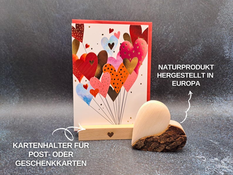 May include: A greeting card with a red border and a colourful heart design, displayed in a wooden card holder. A wooden heart-shaped decoration with bark is next to the card. Text on the card holder reads "Kartenhalter f&uuml;r Post- oder Geschenkkarten".